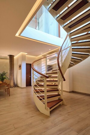 Un escalier moderne en colimaçon, avec des marches en bois et des rampes en métal, menant à un étage supérieur doté d’une lucarne.