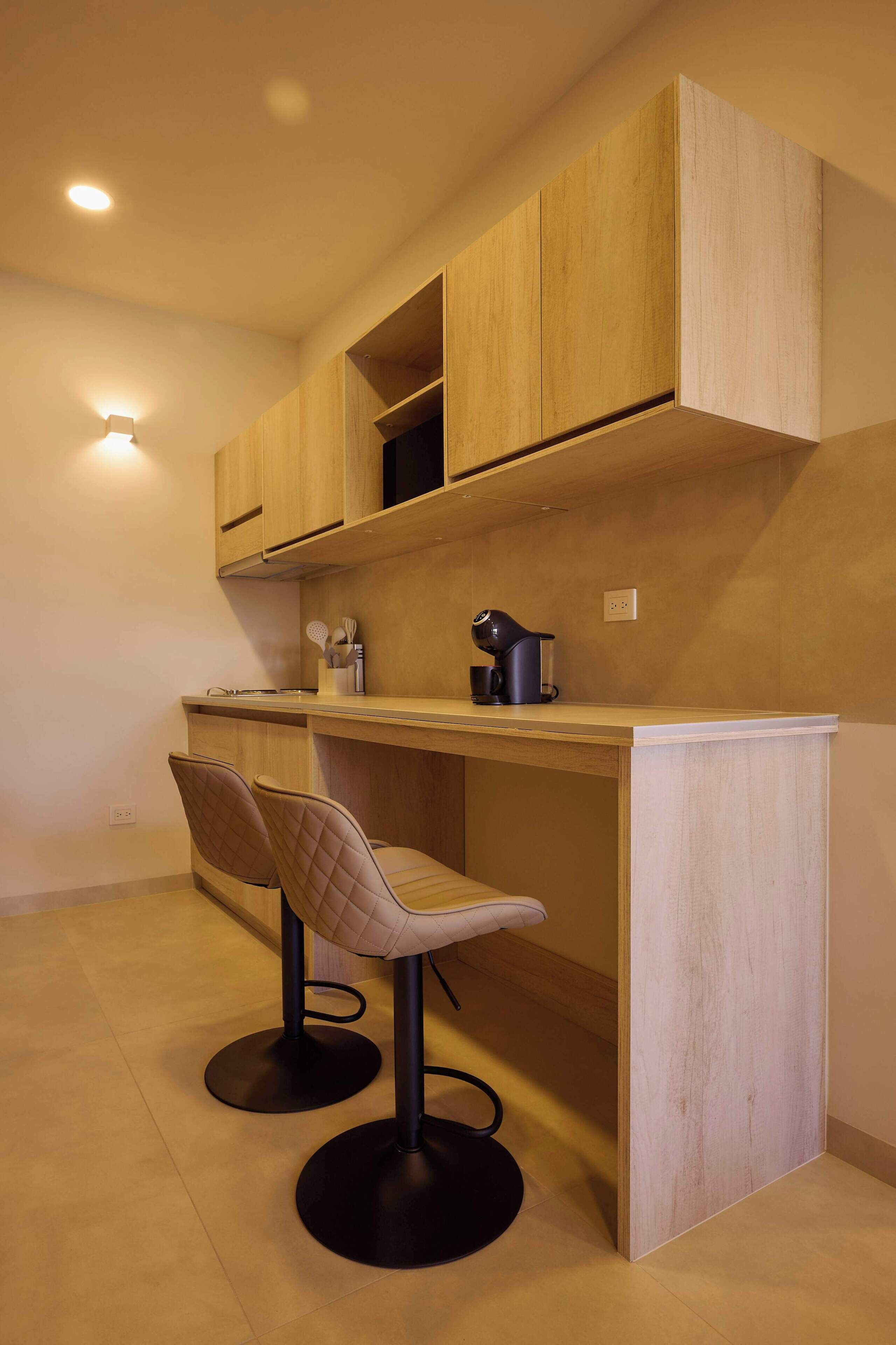 Une cuisine compacte avec des meubles en bois, une machine à café et deux tabourets de bar.
