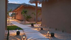 Ein Weg durch ein Resort mit strohgedeckten Gebäuden, Palmen und Wüstenkaktussen.