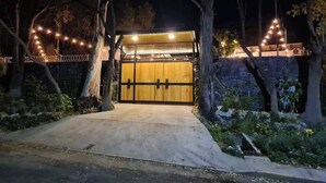 A gated entrance with a wooden door, surrounded by trees and illuminated by string lights.