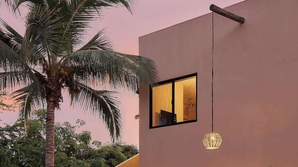 A modern two-story building with a staircase leading to the upper floor, a palm tree, and potted plants on the ground level. - Comfortable Apartment with Pool & Outdoor Oasis (Puerto Escondido)