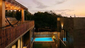 A modern outdoor pool area with a wooden deck, a concrete wall, and a view of the surrounding landscape. - Boutique Retreat Near Beach w/ Pool & Garden (Puerto Escondido)