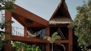 A modern building with a thatched roof, a balcony, and lush greenery. - 200m to beach Casa Caimán w/ Private Pool & Tranquility (Puerto Escondido)