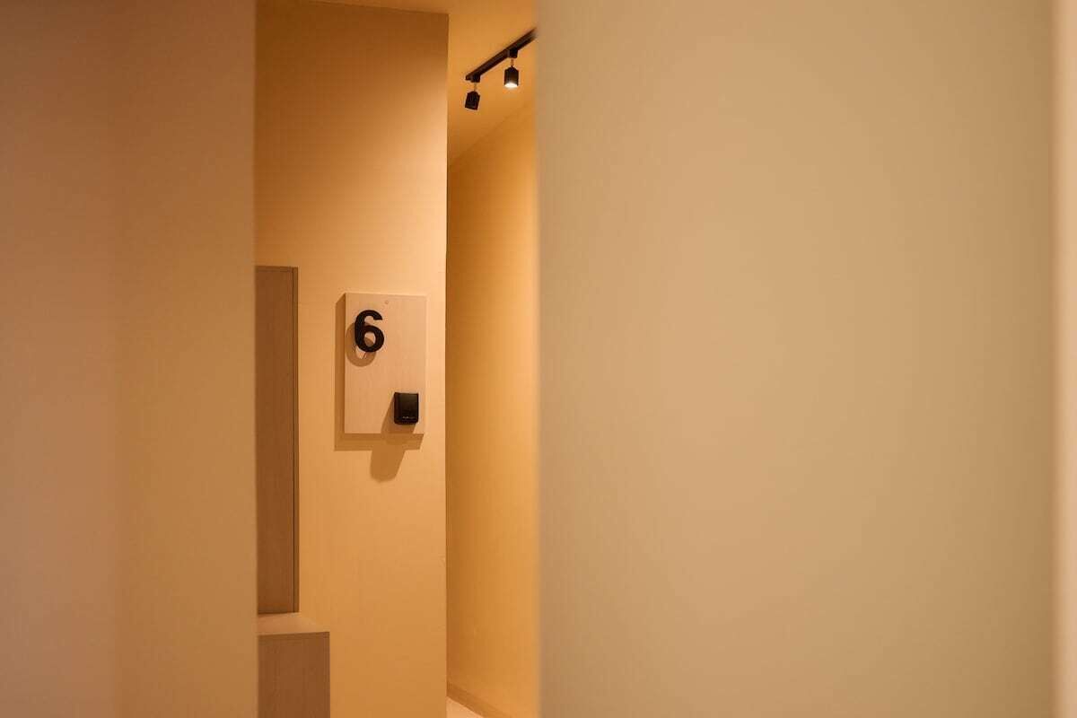 A hallway with a wall-mounted number sign indicating room 6, a light fixture, and a door frame.