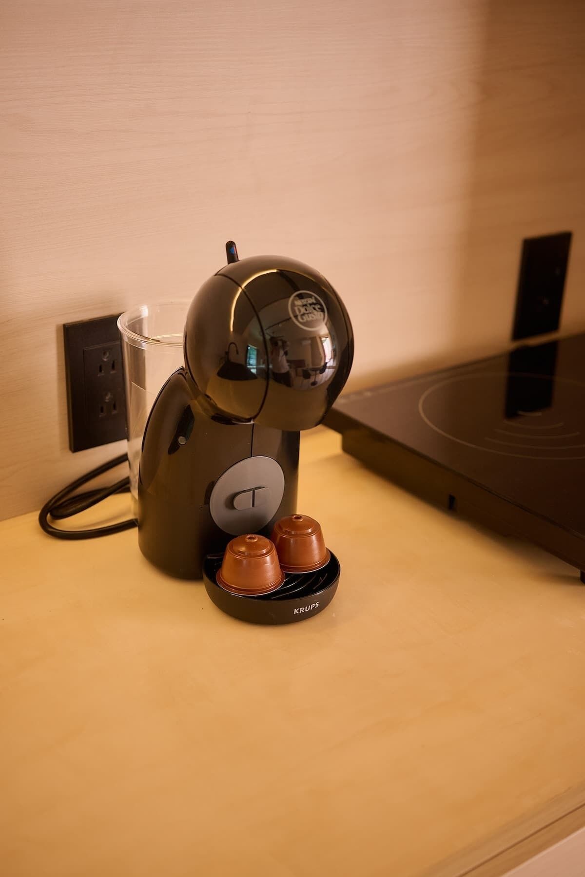 Eine Kaffeemaschine mit zwei Tassen auf einem Holztisch, eine Steckdose und eine Wandsteckdose.