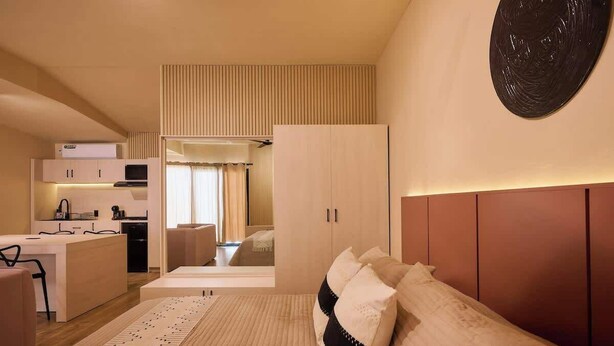 A modern bedroom with a bed, a bedside table, a wardrobe, and a kitchen area in the background. - Stylish King Apartment in Oaxaca's Reforma District (Oaxaca de Juárez)