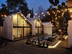 A modern outdoor pool area with two glass-enclosed structures, string lights, and a tree. - !VILLA #6 (1) · Casa Samadhi - Villa #6 Vinaya (Atlixco)