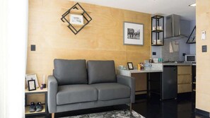Una sala de estar moderna con un sofá gris, una pequeña mesa de centro y una cocina con estufa y armarios.