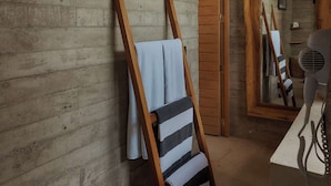 Une pièce aux murs en bois, avec un miroir à cadre en bois, une chaise recouverte d’une serviette à rayures et un sèche-cheveux posé sur une table.