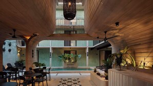 Un vaste espace intérieur comprenant un comptoir d’accueil, des espaces de détente et une piscine centrale.