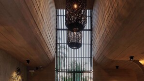 Un espace d’accueil avec un comptoir en bois, un coin salon avec des chaises, un sol à motifs et une grande fenêtre donnant sur un paysage verdoyant.