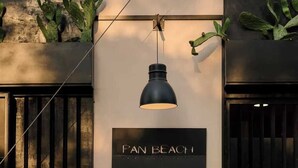 Facciata di un edificio con un cartello che riporta 'PAN BEACH', una lampada a sospensione e piante di cactus.