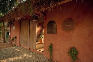 Um edifício rústico com telhado de palha, porta de madeira e uma pequena janela circular.