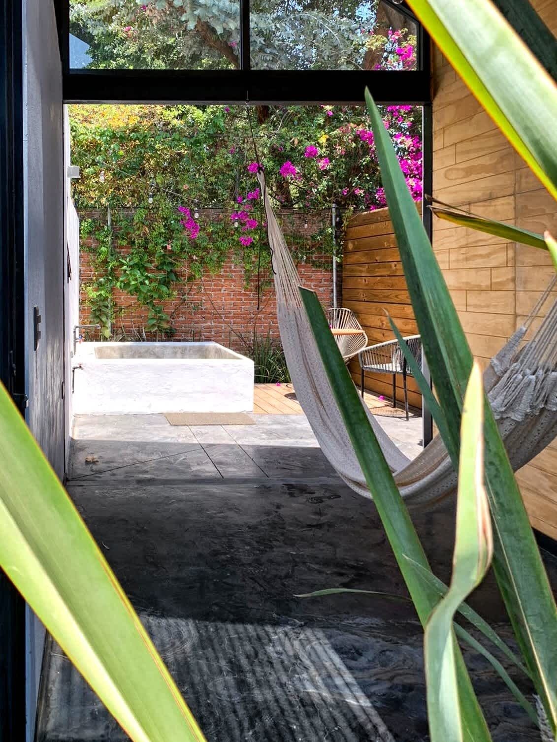 A hammock, a wooden bench, and a brick wall with flowering plants.