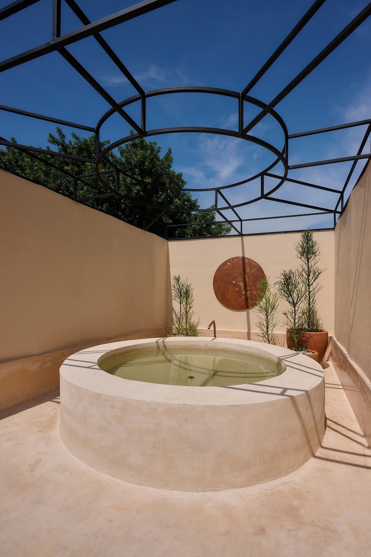 Jacuzzi circular con estructura metálica sobre ella, rodeado de paredes color beige y plantas en macetas.