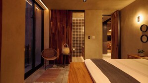 Une chambre à coucher moderne avec un grand lit, un banc en bois, une chaise en osier et une petite table sur laquelle est posée une plante.
