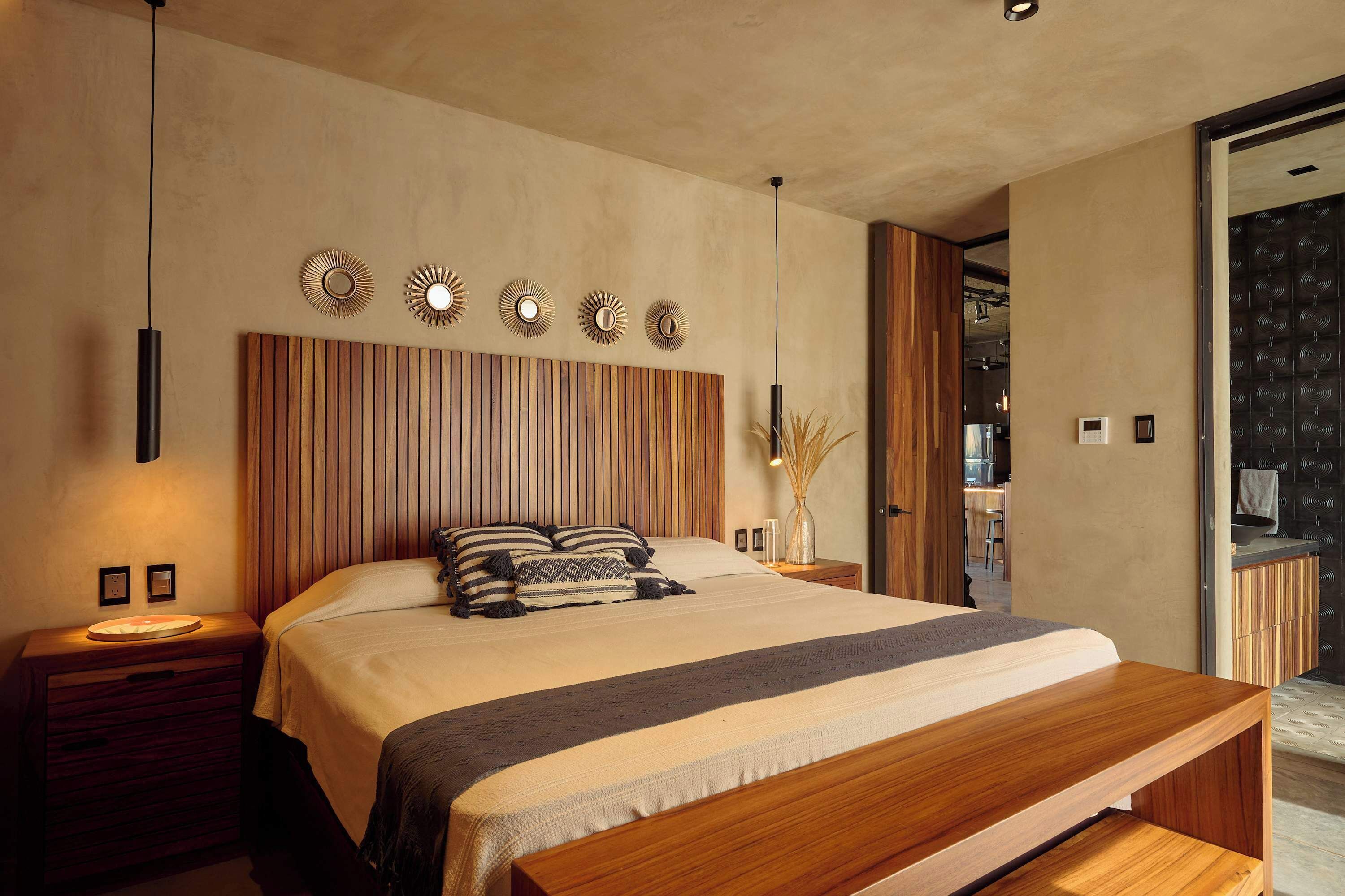 A modern bedroom with a wooden headboard, a large bed, bedside tables, and wall-mounted light fixtures.
