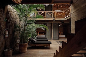 Una terraza de madera con sillones de descanso, una planta grande en maceta y un balcón con techo de paja.