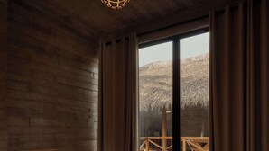 Une pièce de cabane en bois comprenant un lit, un luminaire suspendu et donnant sur une terrasse en bois à l’extérieur.