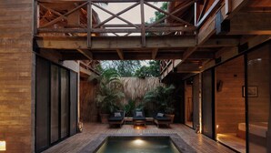 Un espace piscine moderne avec une terrasse en bois, des chaises longues et un mur recouvert de chaume.