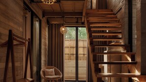 Un intérieur en bois avec un escalier, un luminaire suspendu et une chaise en osier.