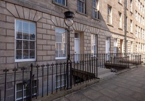 A building with a stone facade, multiple windows, and a black wrought iron fence. - Elegant historic Edinburgh apartment with space for ten in a prime city location (Edinburgh)