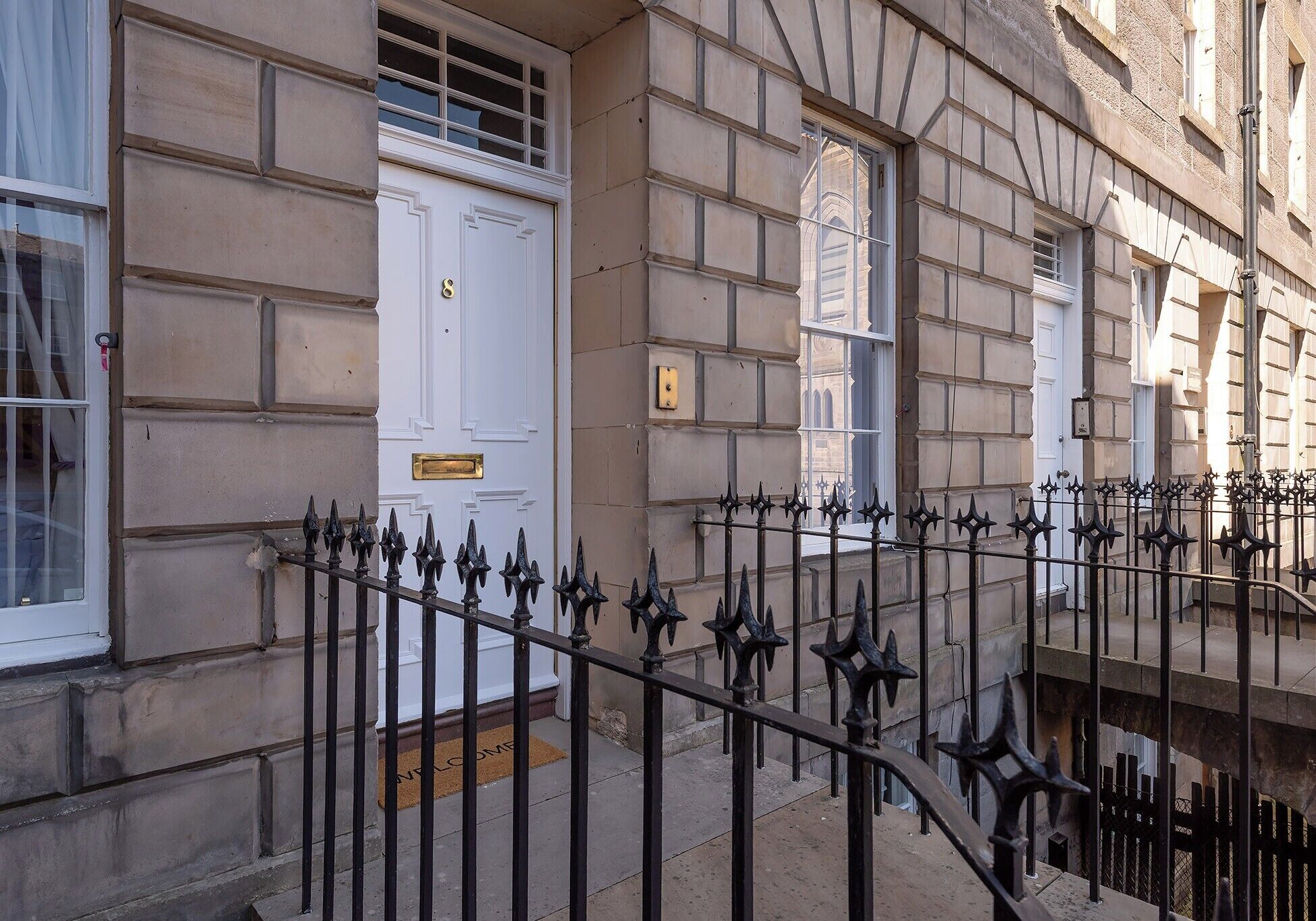 A building facade with a white door, a doormat, and a black wrought iron fence.