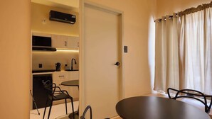 A compact room with a dining table, chairs, a kitchen area with cabinets and appliances, and a window with curtains. - Stylish King Apartment in Oaxaca's Reforma District (Oaxaca de Juárez)