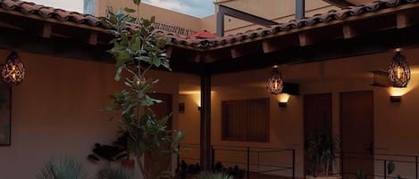 A courtyard with potted plants, a pergola, and a building with a tiled roof.