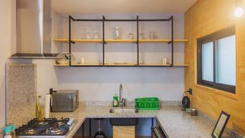 A compact kitchen with a gas stove, microwave, and wooden shelves above the sink.