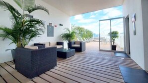 Et moderne udendørs loungeområde med fletningsmøbler, krukker med planter og en træterrasse.