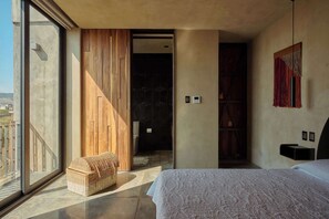A modern bedroom with a large bed, a wooden bench, and a view of the outdoors through a large window. - Stylish Apartment w/ Hot Tub & Mountain Views (Oaxaca de Juárez)