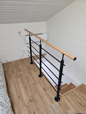 Un escalier avec une main courante en bois, des rampes en métal noir et un mur blanc muni d’un thermostat.