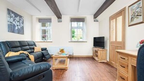 Una sala de estar con sofá de cuero negro, una mesa de centro de madera y un televisor sobre un mueble bajo.