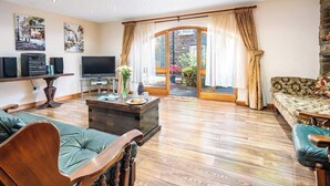 A spacious living room with a television, speakers, and a coffee table. There is a sofa and a chair, and a large window with curtains. - Weavers Rest offers beautifully crafted accommodation in a magnificent area of Wales (Llandysul)