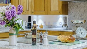 A kitchen counter with a vase of flowers, a coffee maker, a bread loaf, spice jars, and a kitchen scale. - Weavers Rest offers beautifully crafted accommodation in a magnificent area of Wales (Llandysul)