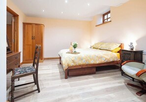A bedroom with a bed, wooden wardrobe, chair, and a small table with a bottle and flowers.