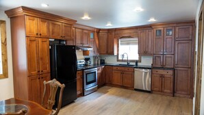 A kitchen with wooden cabinets, a black refrigerator, stainless steel appliances, and a dining area with a glass table and wooden chairs.