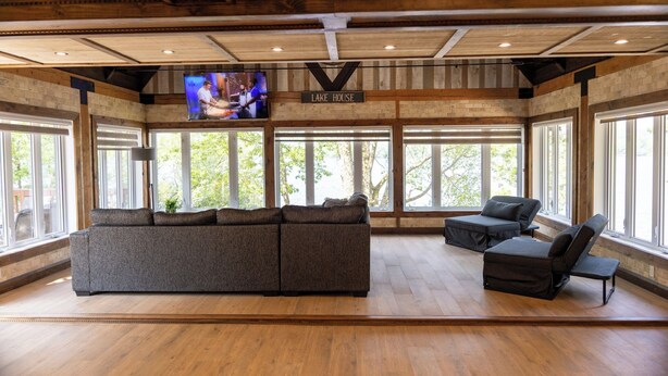 A spacious room with a large sectional sofa, a recliner, and a TV screen displaying a cooking show.