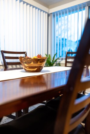 A dining table with a bowl of fruit, two chairs, and a window with blinds.