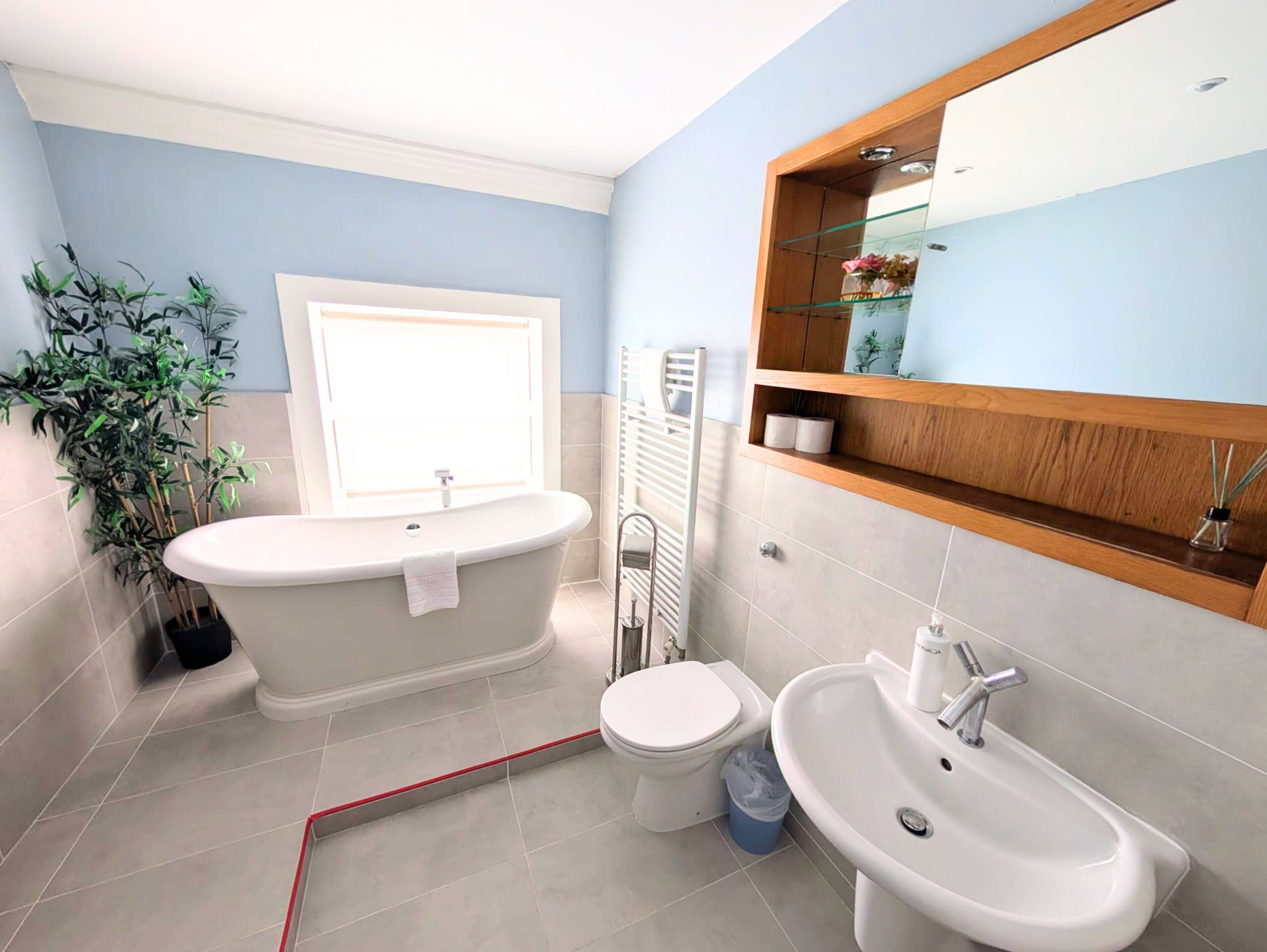 Ein Badezimmer mit freistehender Badewanne, Toilette, Waschbecken und Fenster.