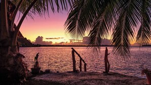 A beach scene with palm trees, a wooden structure, and a sunset over water. - PARADISE II (Bora Bora)