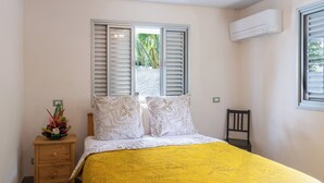 A bedroom with a bed, a nightstand, a chair, and a window with shutters. - PARADISE II (Bora Bora)