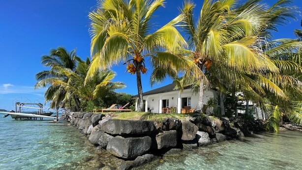 A beachfront property with clear water, palm trees, and a boat dock. - PARADISE II (Bora Bora)