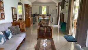 A spacious living area with a sofa, a coffee table, and a dining table with chairs. There is a kitchen in the background with a refrigerator and a microwave. - PARADISE II (Bora Bora)