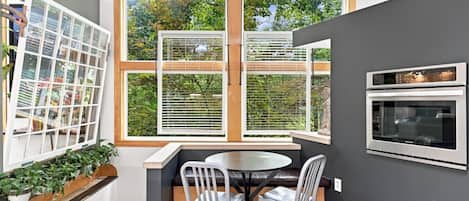 A modern kitchen with a built-in oven, a dining table with chairs, and a window with blinds.