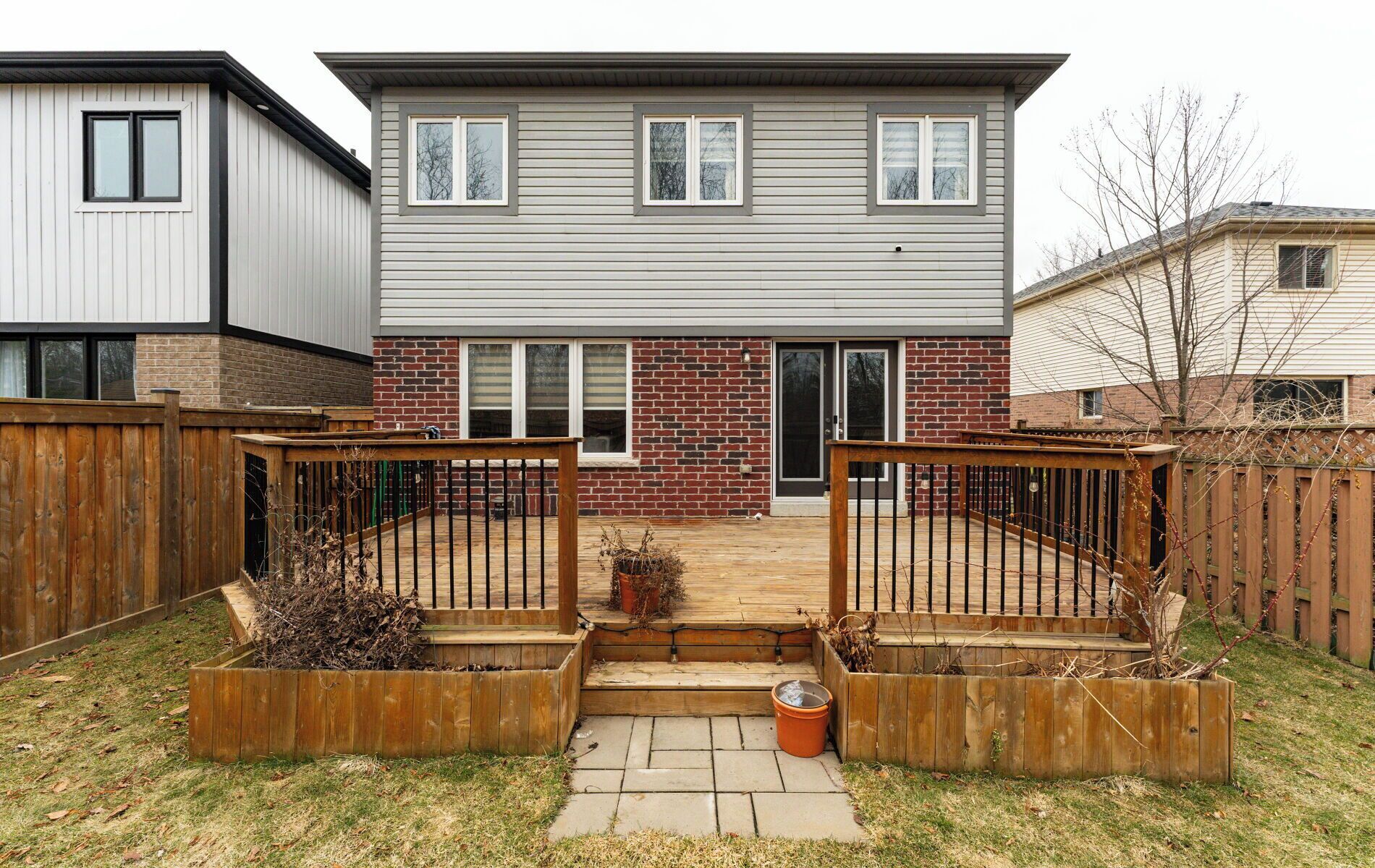 A two-story residential building with a brick facade, a front door, and a small front yard with a wooden deck and planters.
