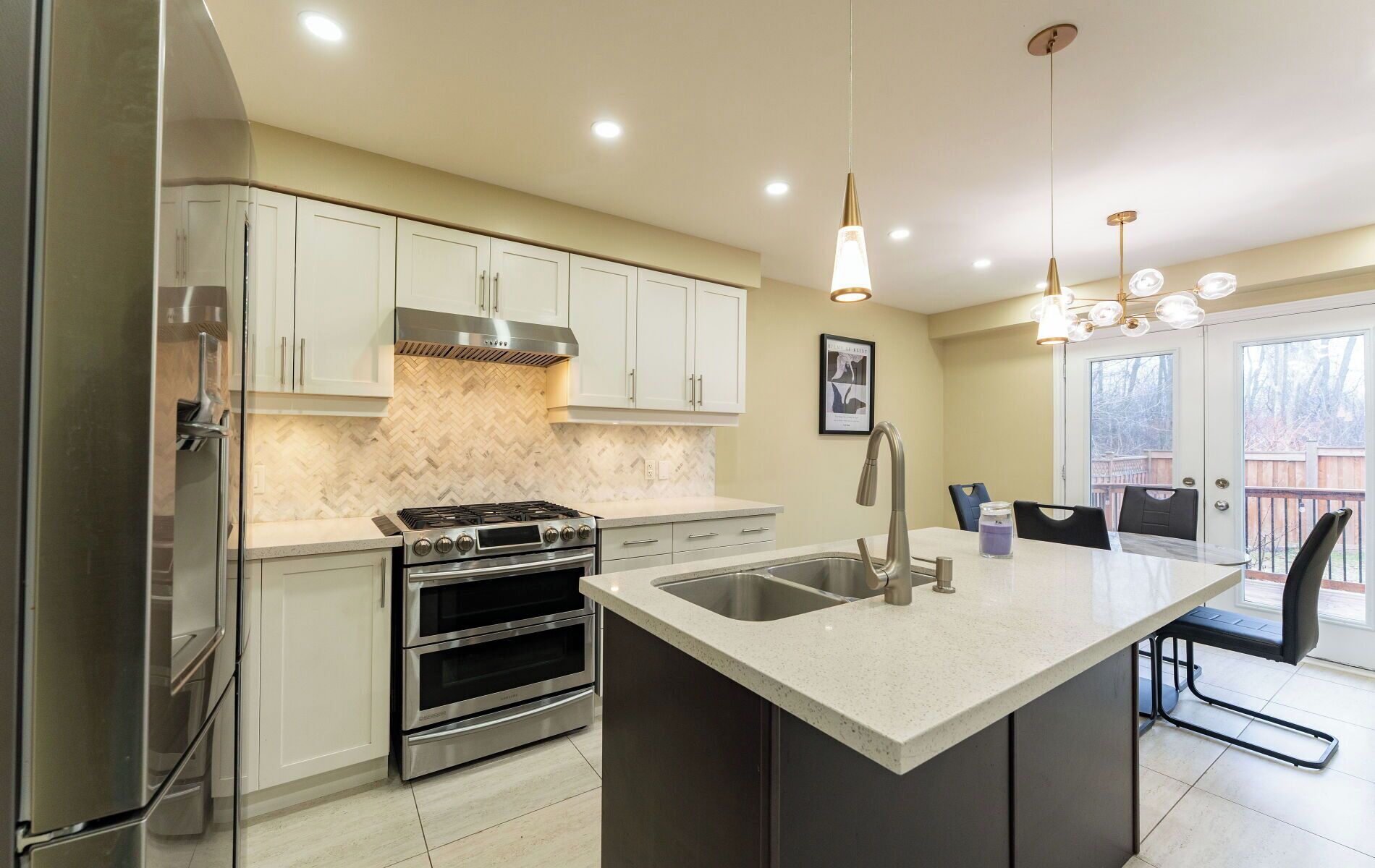 A modern kitchen with stainless steel appliances, a herringbone tile backsplash, and a large island with a sink.