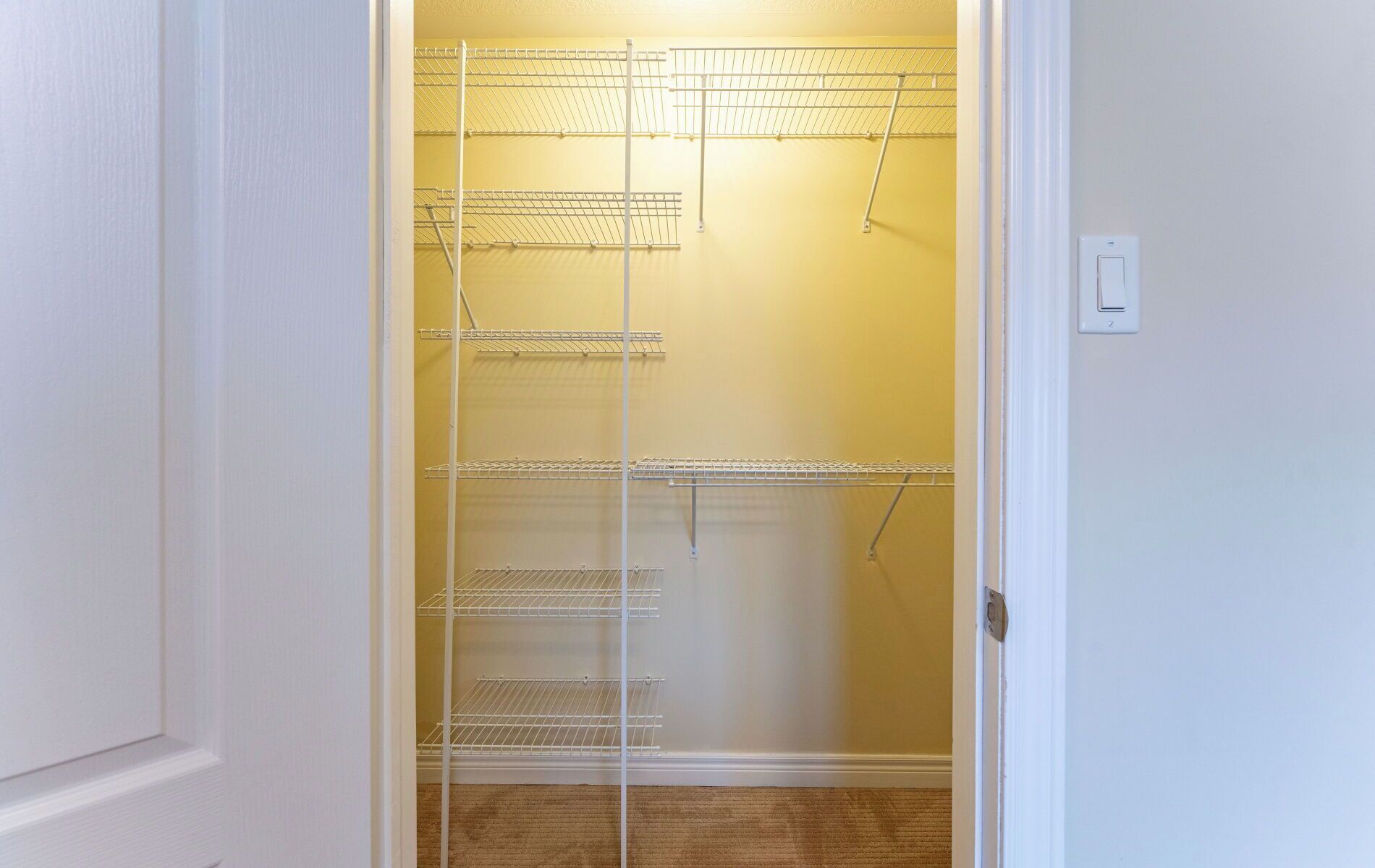 A walk-in closet with multiple wire shelves and a door with a light switch.