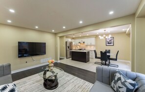 A modern living room with a flat-screen TV, a glass coffee table, and a sofa with patterned cushions.